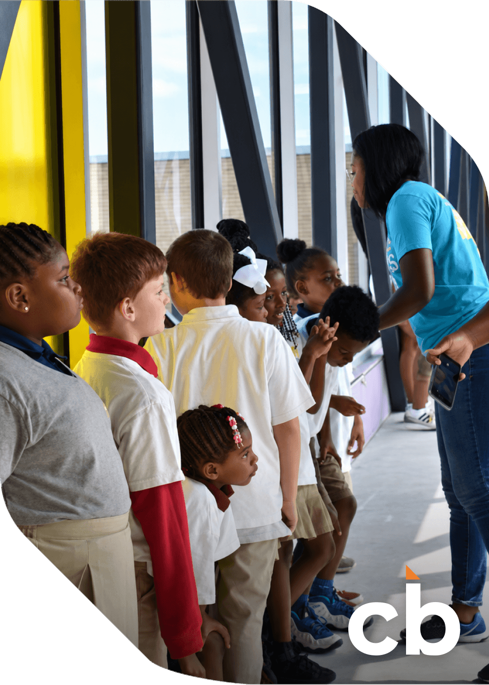 A Central Bank of Kansas City employee talks with a group of schoolchildren lined up along a bright window
